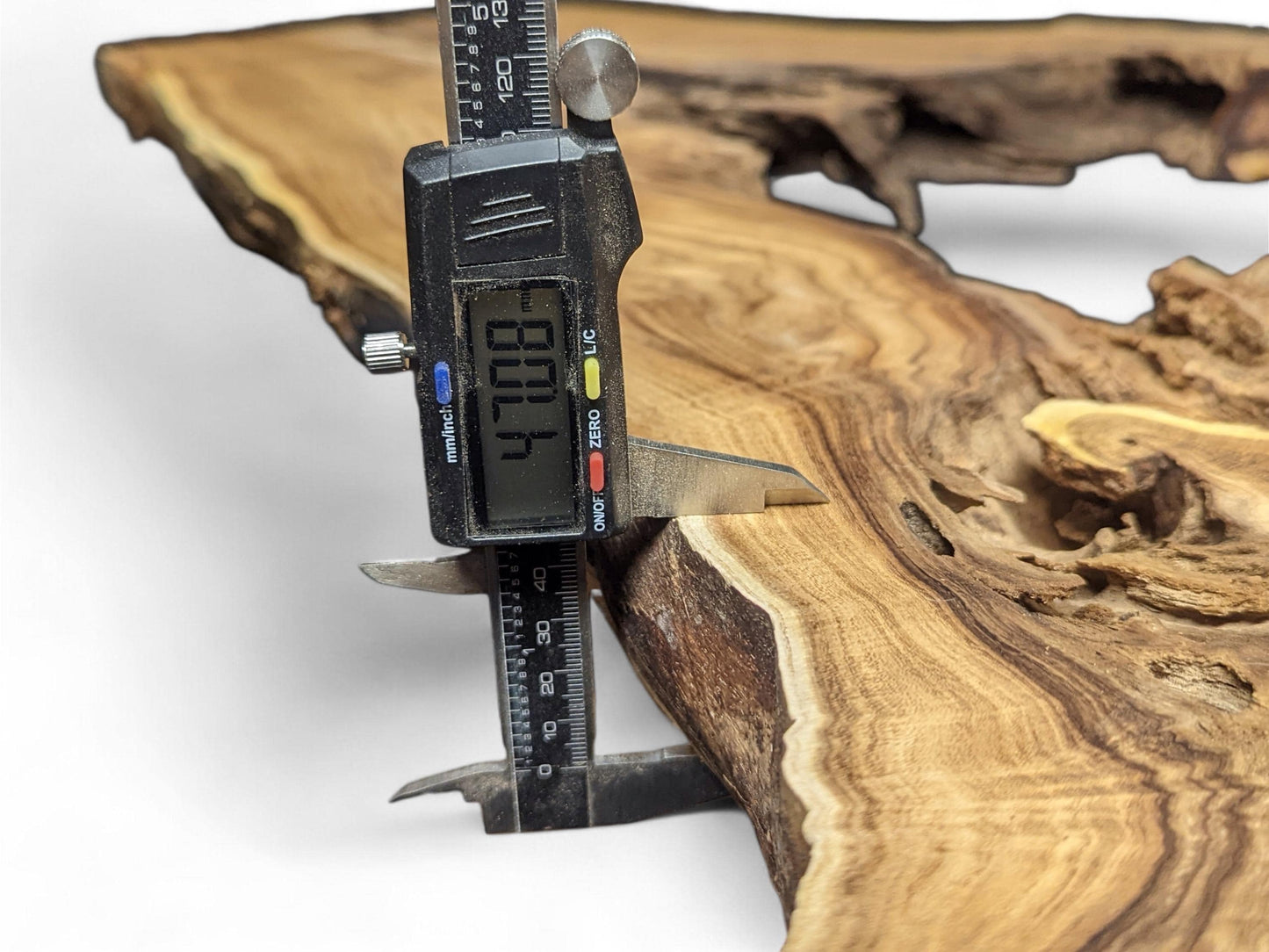 A digital caliper measures the 47.08mm thickness of a light brown wood root slice with dark grain.