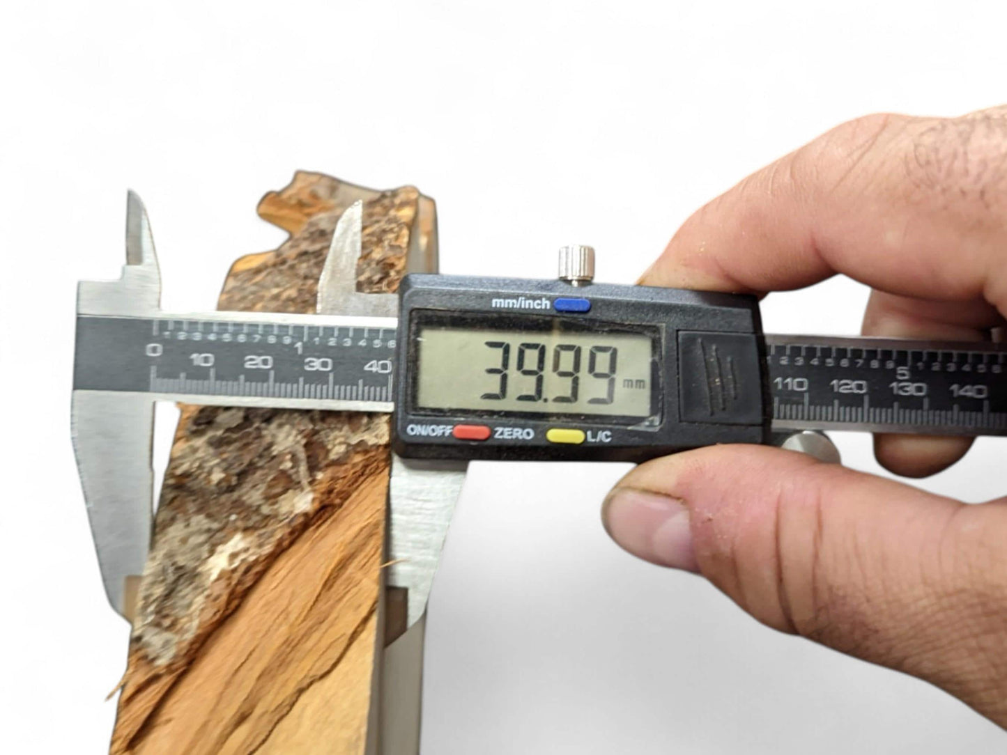 A digital caliper held by a hand measures a rough bark wood slice at 39.99 mm.
