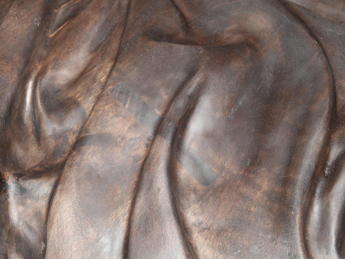 Textured dark brown walnut wood carving showing undulating folds and two rectangular repairs.
