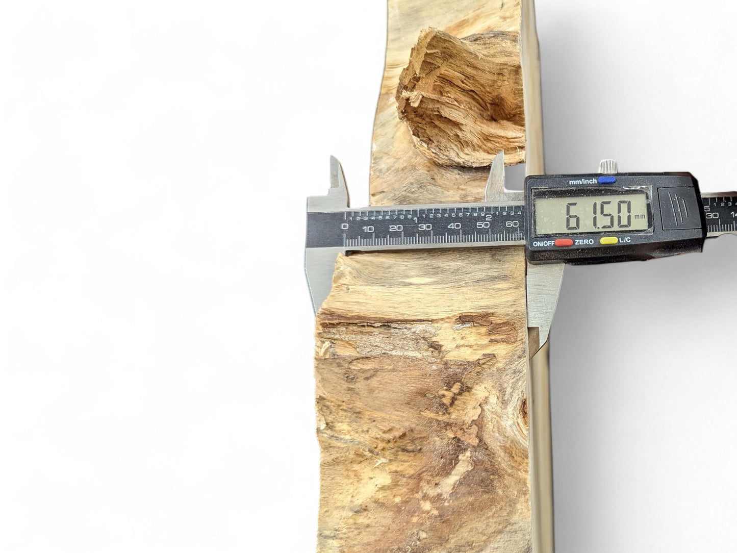 Digital caliper measures a light brown wood piece, showing 61.50mm with prominent grain and a rough edge.