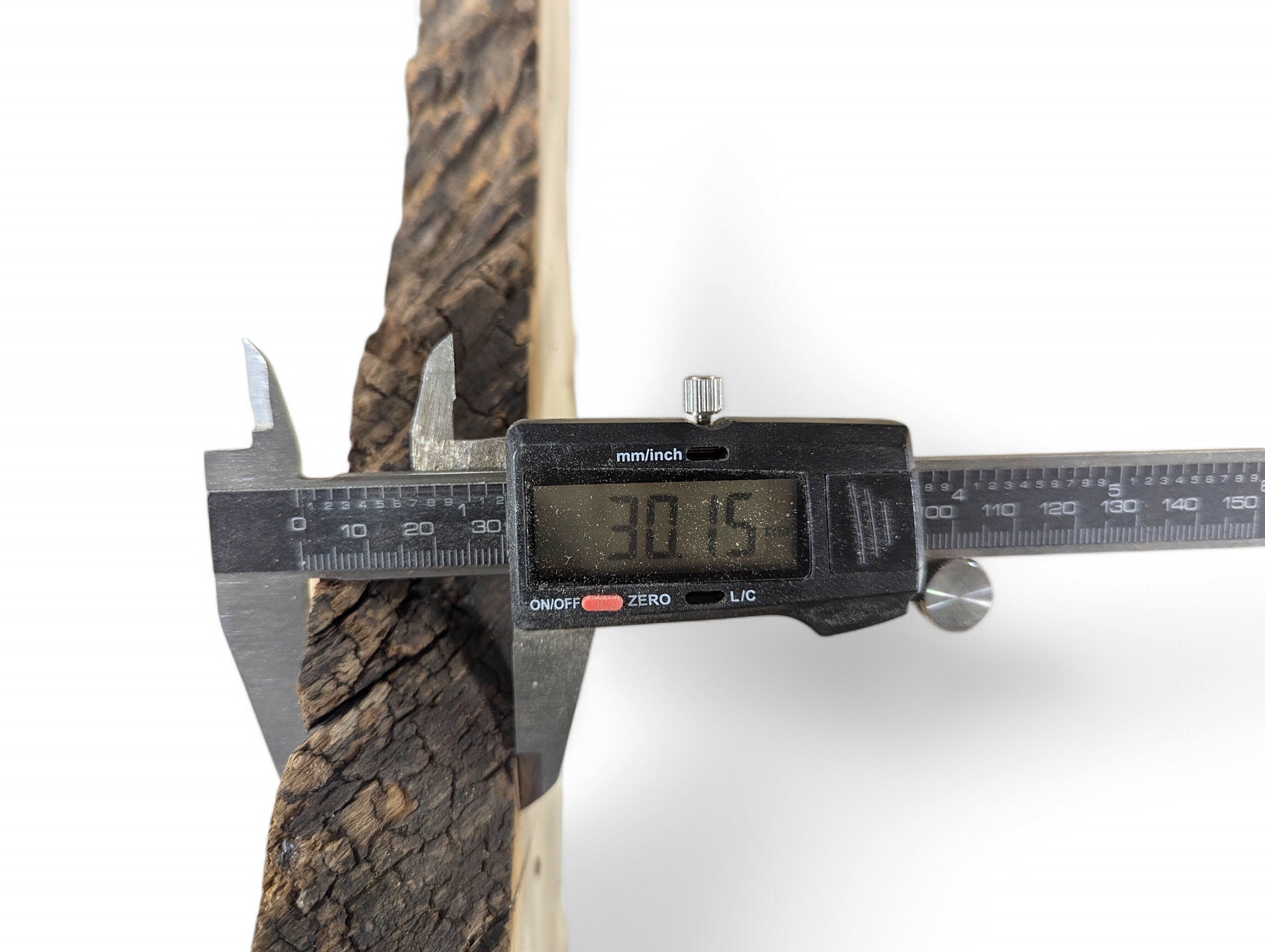 Digital caliper measuring a black locust root wood slice, showing dark bark and light wood at 30.15mm.