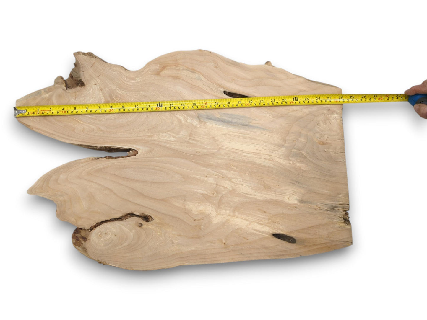 A yellow tape measure is held across a pale, freeform wood slab with flowing grain.