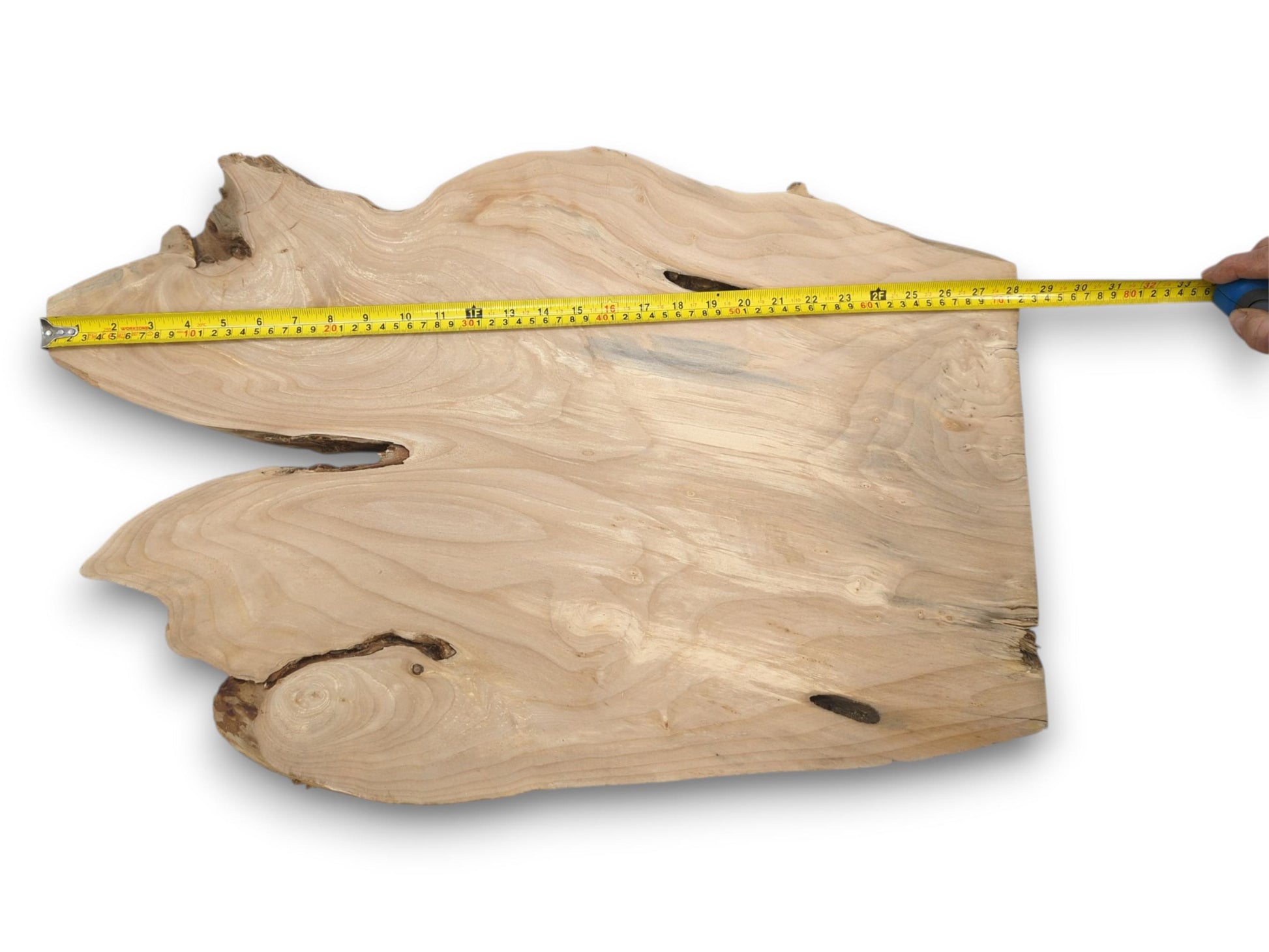 A yellow tape measure is held across a pale, freeform wood slab with flowing grain.