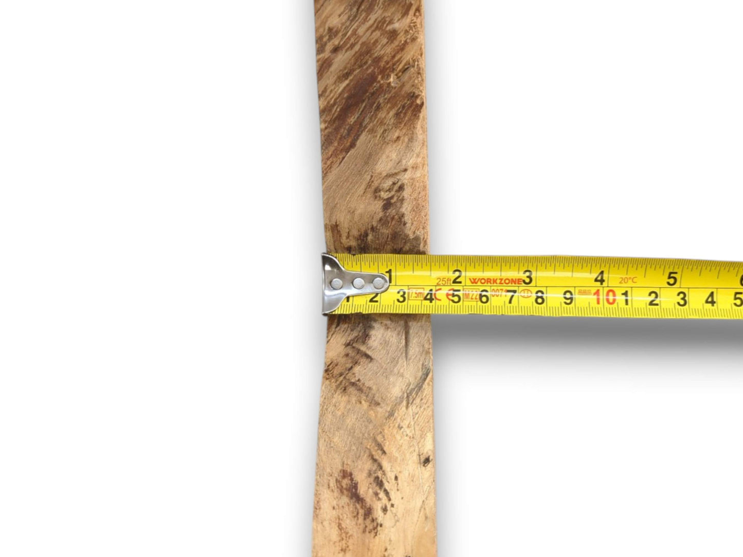 A yellow tape measure gauges the width of a narrow, rustic timber with mottled grain.