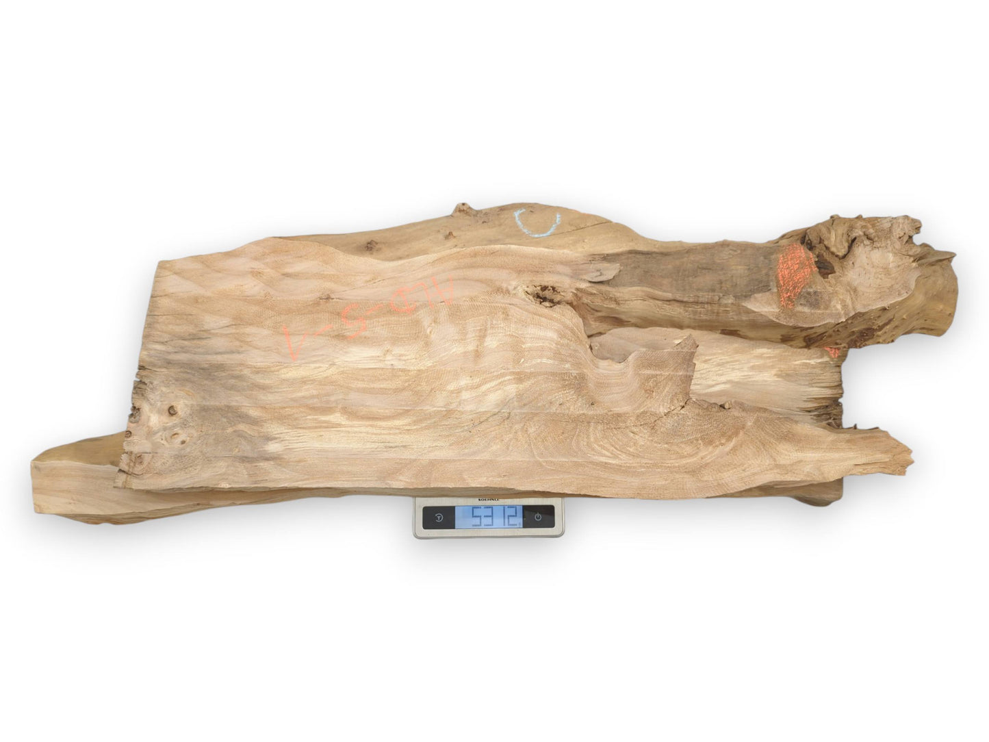 An irregular timber slab with wavy grain and chalk marks rests on a digital scale.