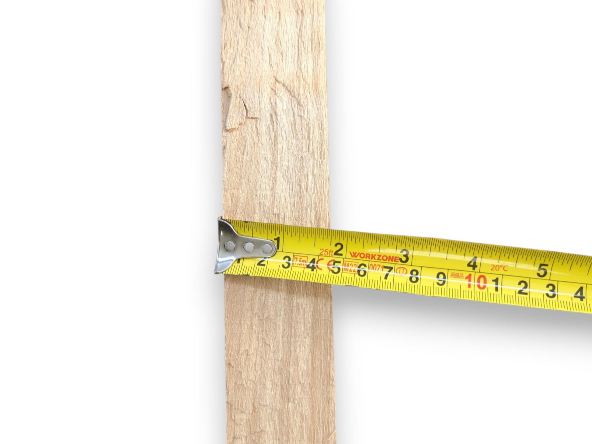 A yellow tape measure gauges the width of a vertical, rough-sawn plank of wood.