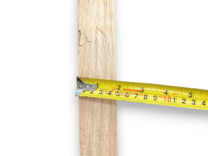 A yellow tape measure gauges the width of a vertical, rough-sawn plank of wood.