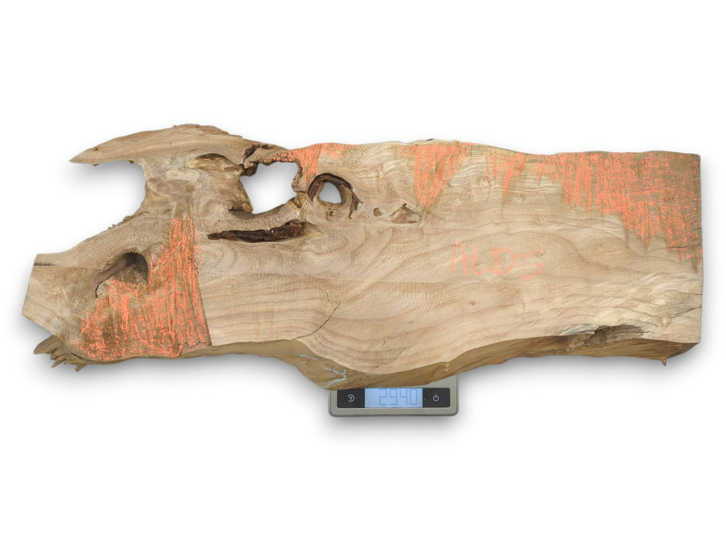 An irregular timber slab with orange highlights and gnarled voids rests on a digital scale.
