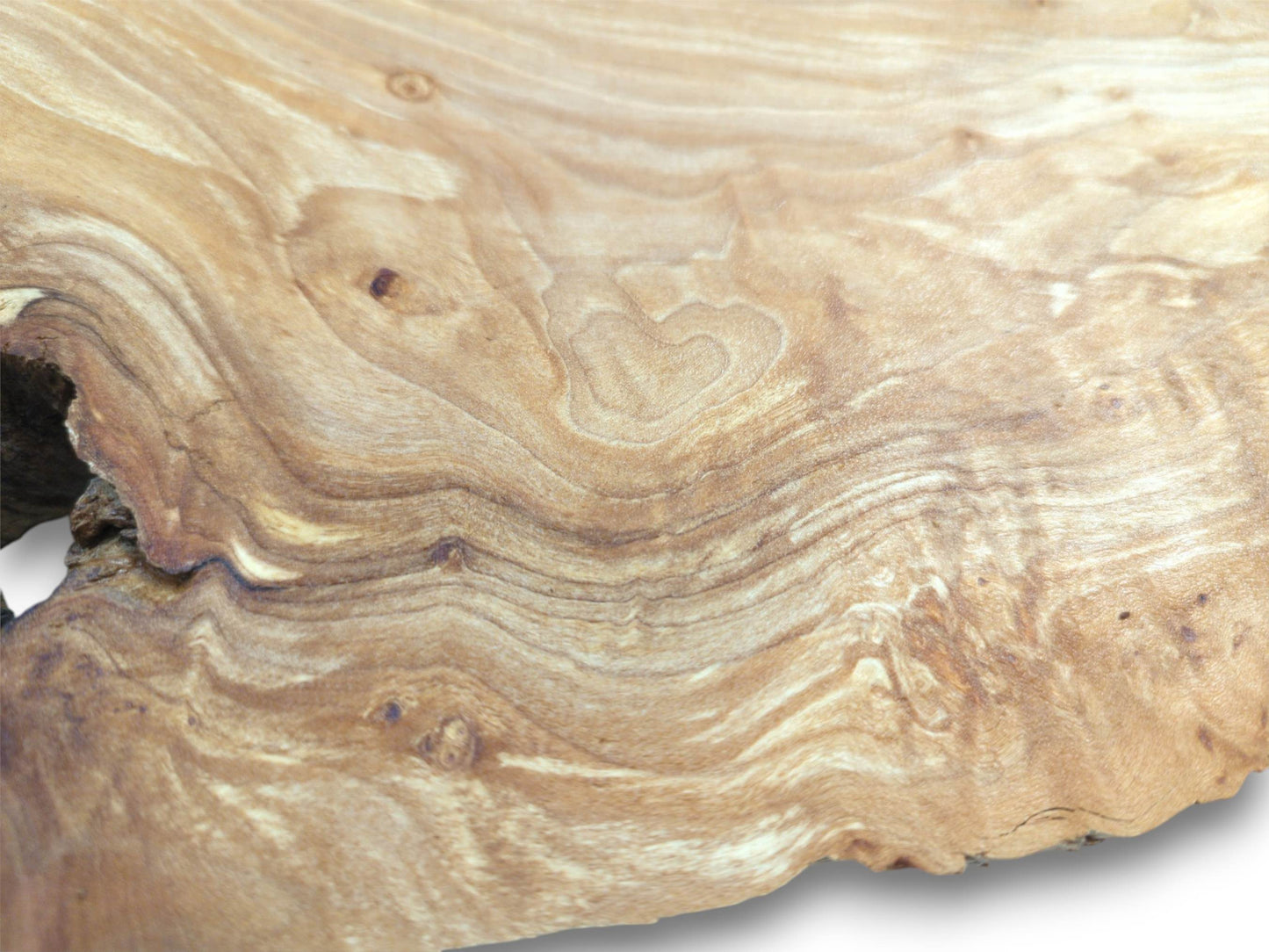 A polished timber surface shows a natural heart shape formed by its flowing, contoured grain.