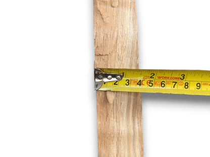 Close-up of a yellow tape measure checking the width of a rough, unfinished wood slat.