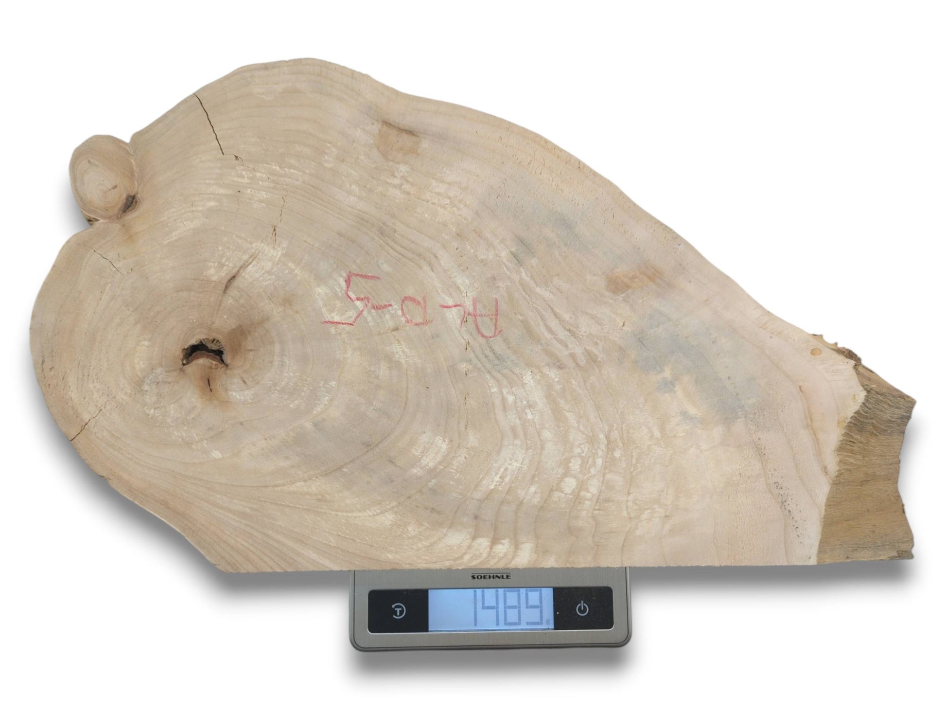 An irregular timber slab with pale grain and red writing rests on a digital scale.