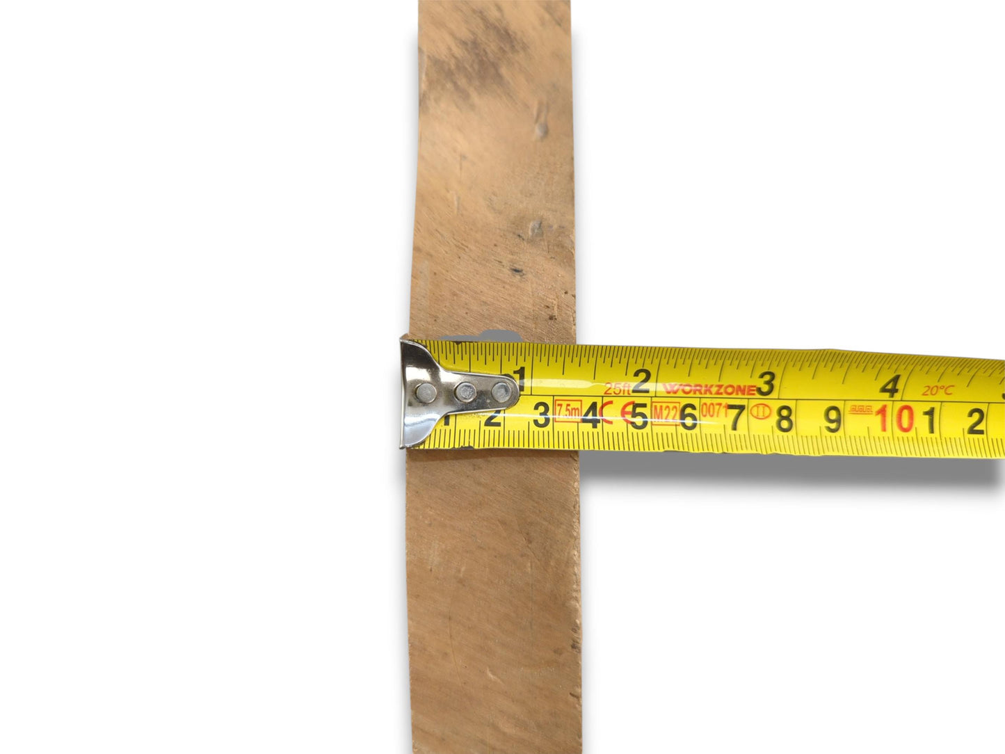 A yellow tape measure is held across a light-toned lumber plank showing its width.