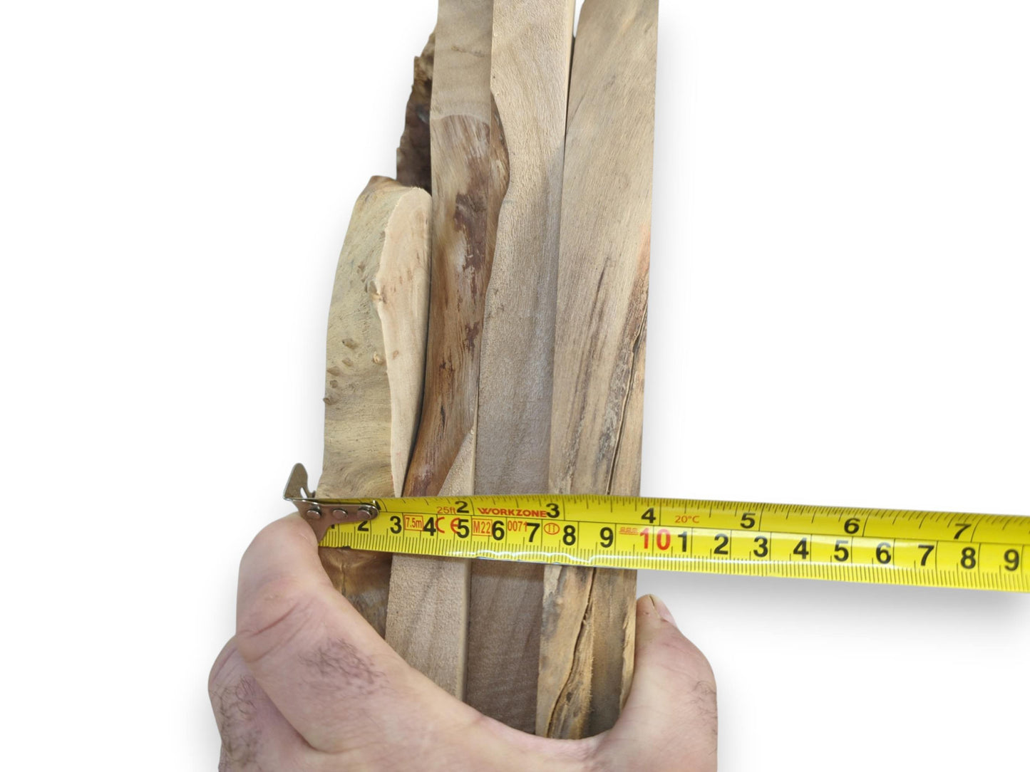 A hand holding a yellow measuring tape against multiple light brown alder wood slabs.