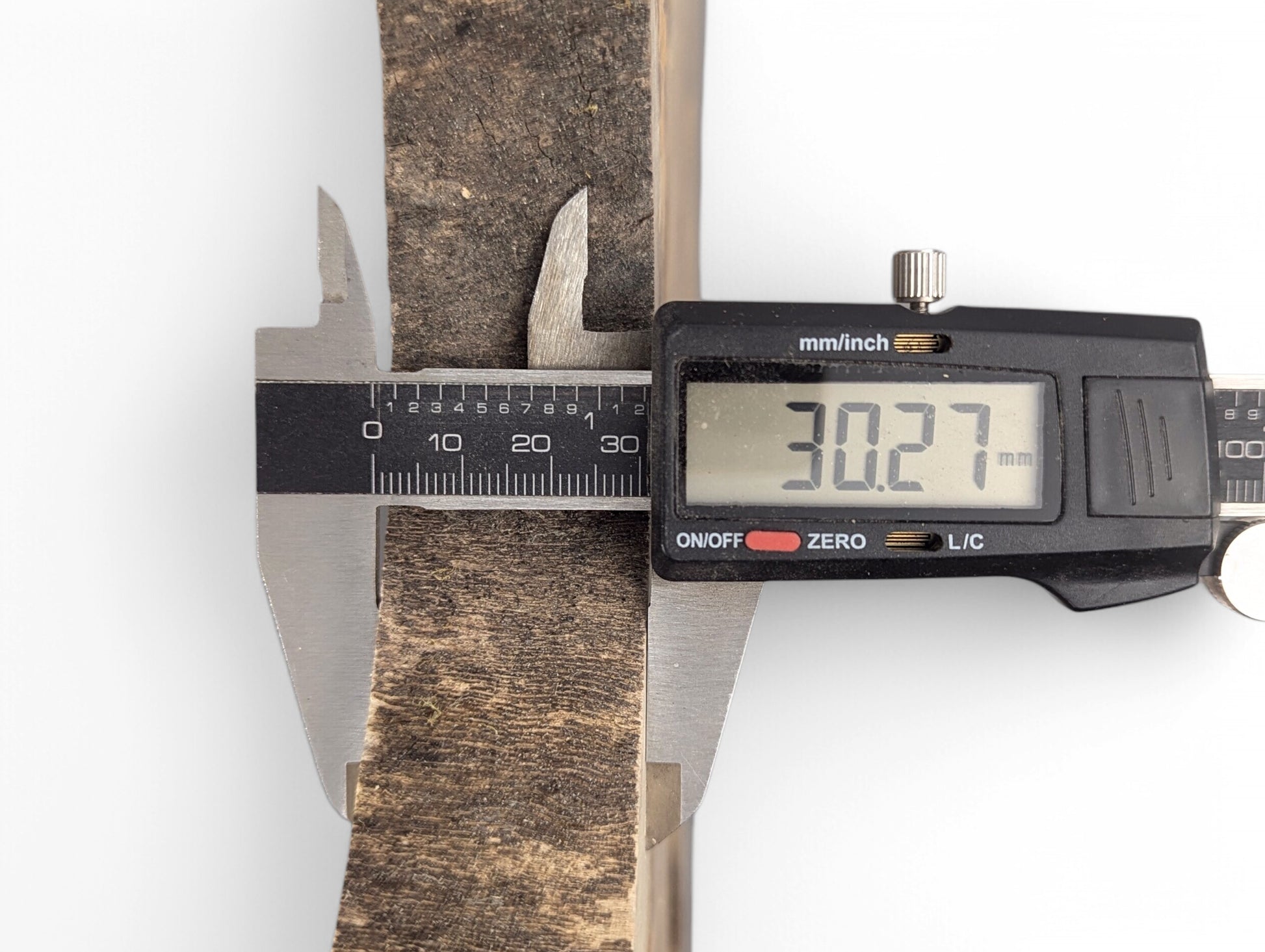 Digital caliper displays 30.27 mm, measuring the thickness of a dark, textured wood slice.
