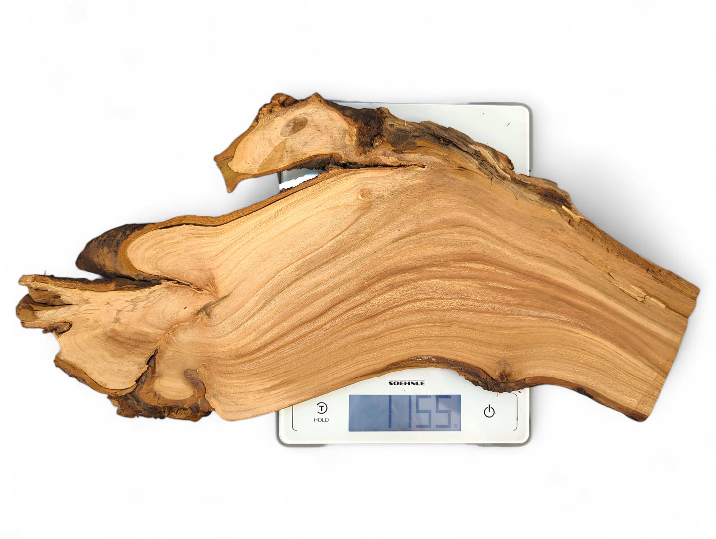 Light reddish-brown cherry root slice with wavy grain and dark live edges on a digital scale displaying 115.5.
