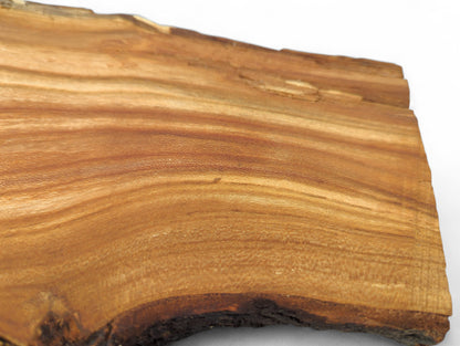 Rustic wood slice with light reddish-brown color, distinct wavy grain, and a dark, textured live edge.