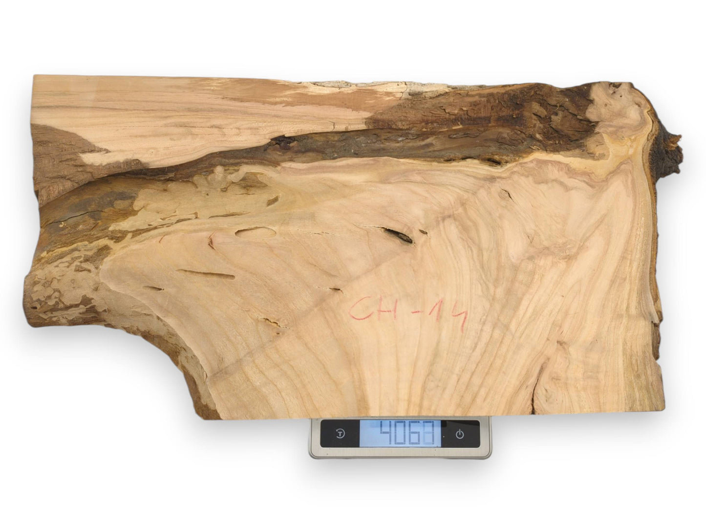 A live edge cherry wood slab with red writing rests on a digital scale showing its weight.