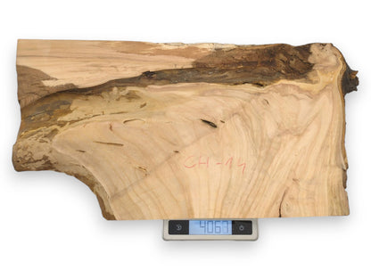 A live edge cherry wood slab with red writing rests on a digital scale showing its weight.