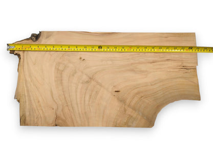 An overhead view of a live edge cherry lumber blank with a tape measure along its length.