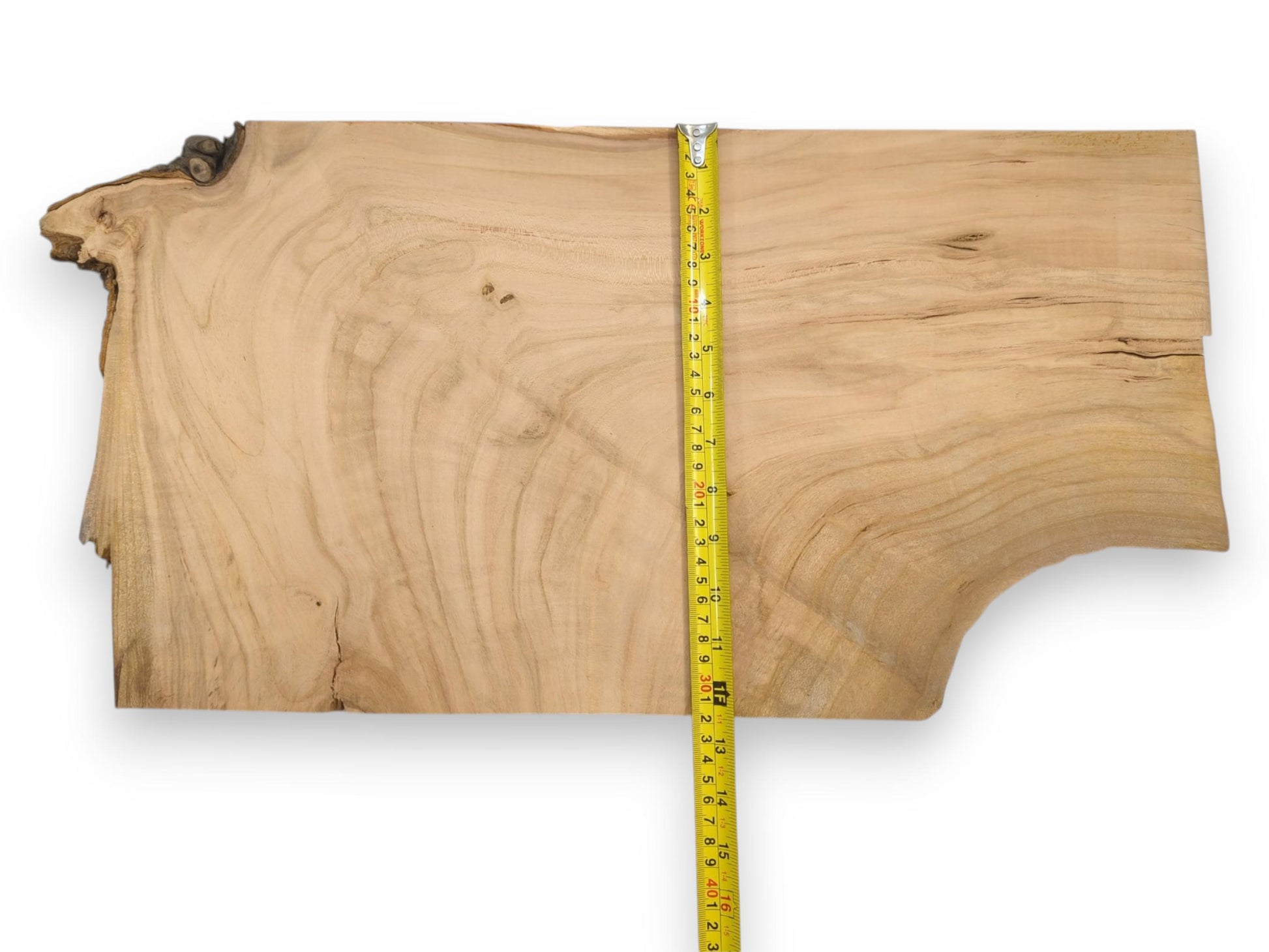 A vertical yellow measuring tape lays across a light cherry wood blank, showing its size and grain.