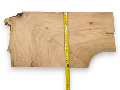 A vertical yellow measuring tape lays across a light cherry wood blank, showing its size and grain.