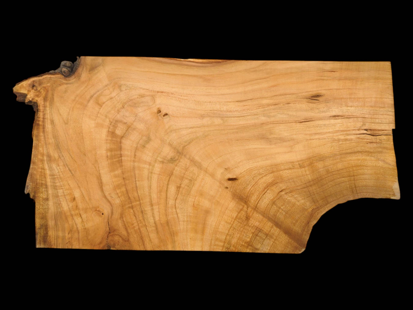 Overhead view of a wild cherry slab featuring a wavy, golden-brown grain and a dark, natural edge.