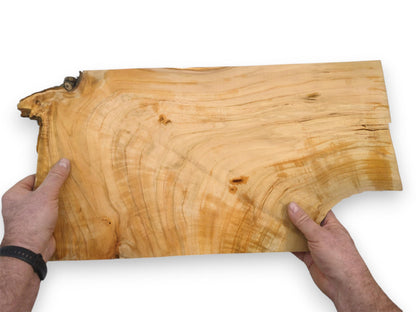 A person's hands display a light-toned wild cherry slab with a sweeping grain and live edge.