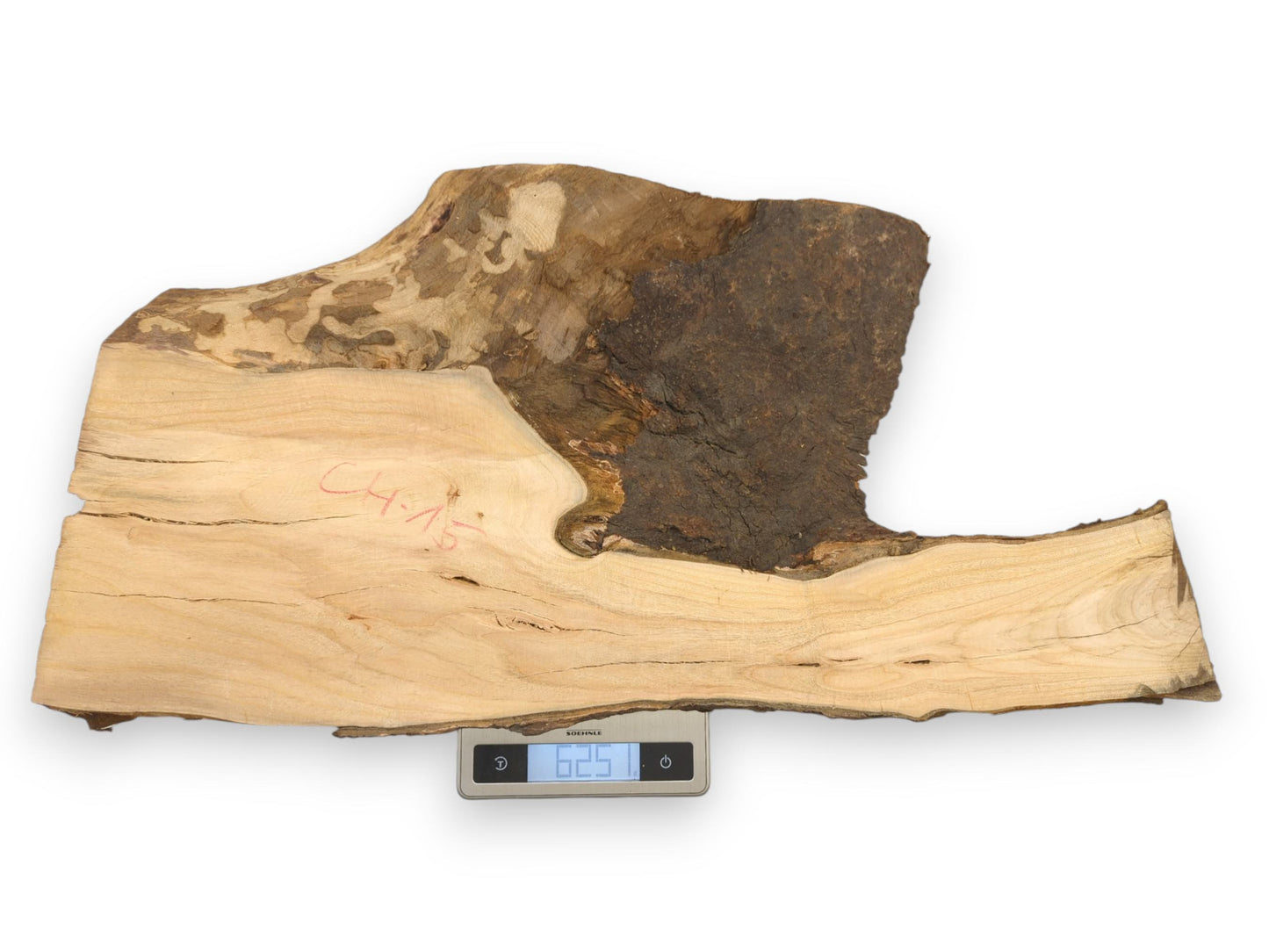 A slab of raw cherry wood with a large bark section rests on a digital weighing scale.
