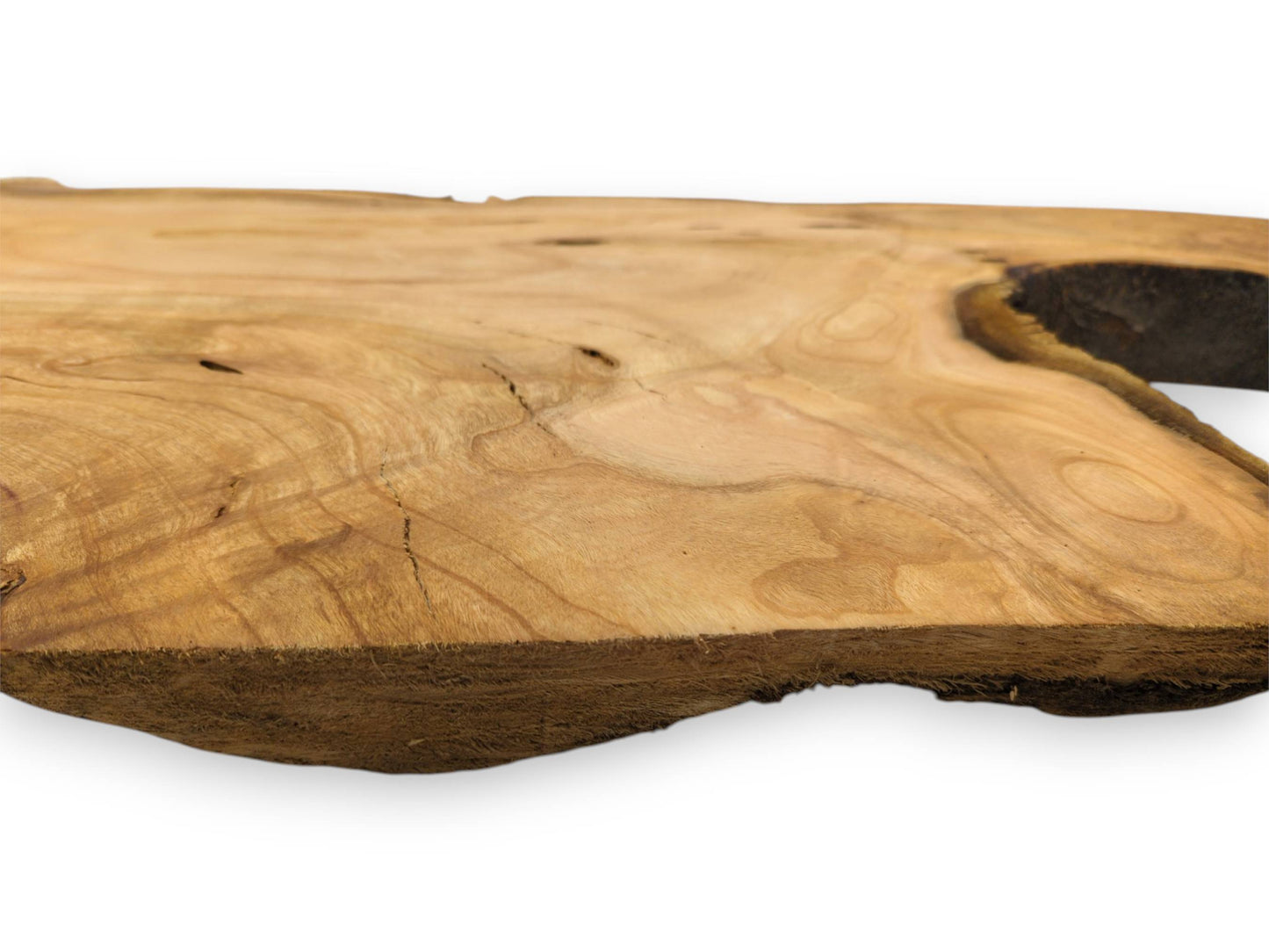 A low-angle shot across a cherry wood slab, showing its golden grain and fibrous front edge.