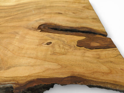 A raw cherry timber slab displaying its wavy, light grain around a dark, hollowed-out knot.