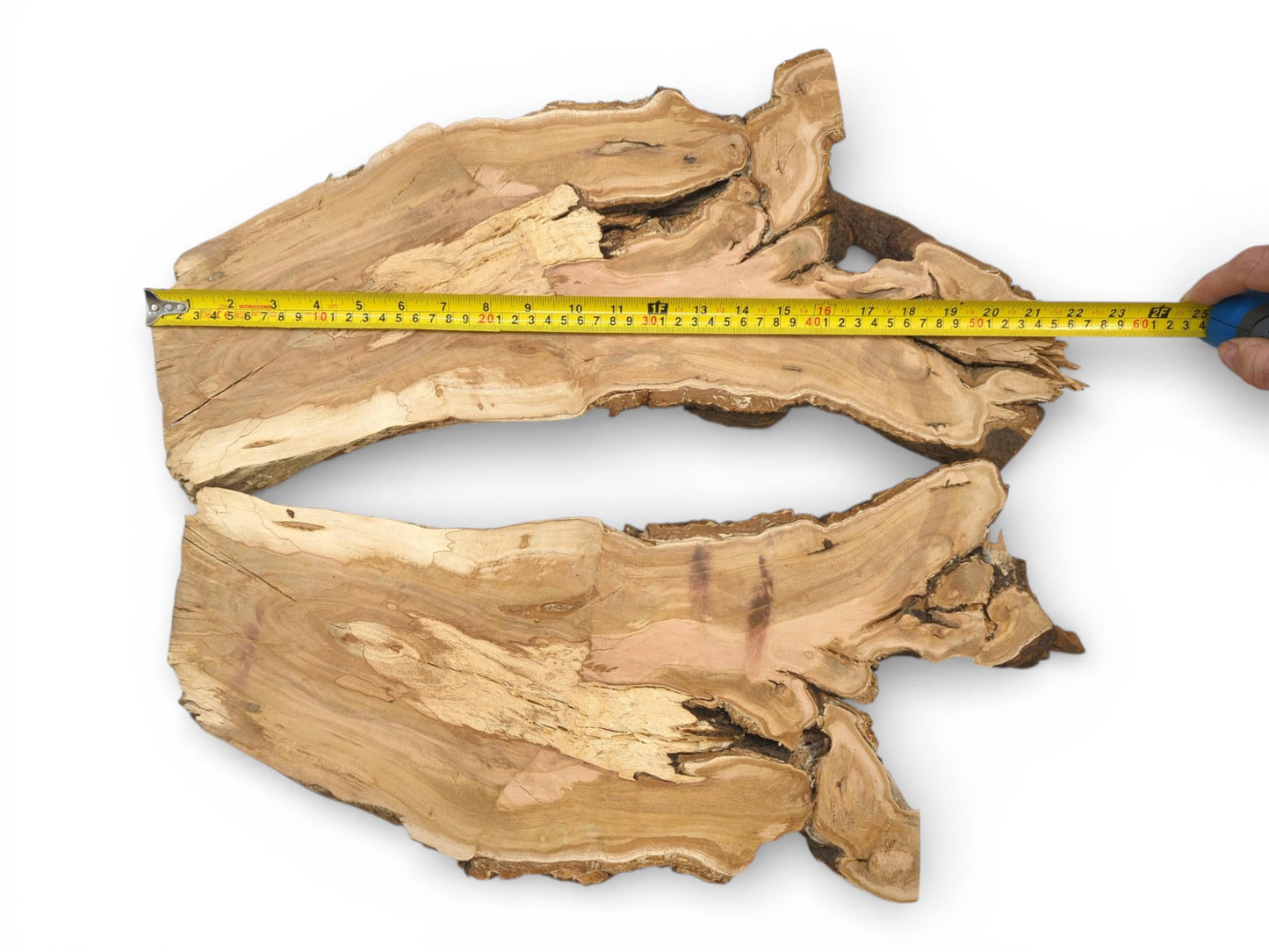 A hand extends a yellow measuring tape to show the width of two unfinished lumber pieces.