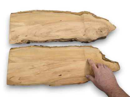 A person's hand points to the wood grain on the lower of two live-edge cherry slabs.