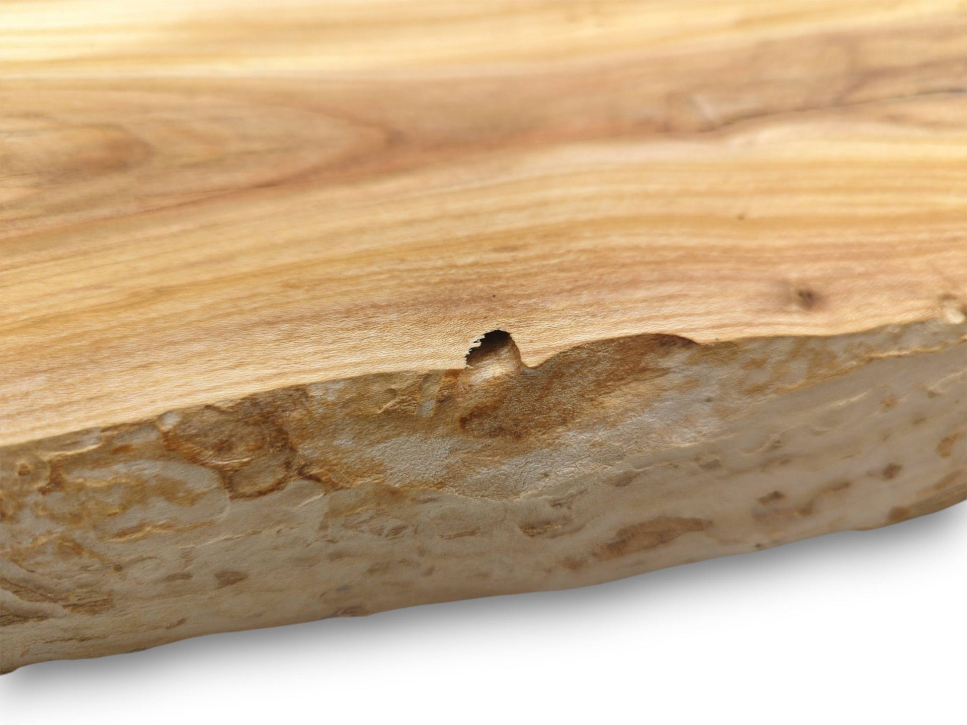 A detailed shot of a wood slab’s live edge, showing its rough texture and a small divot.