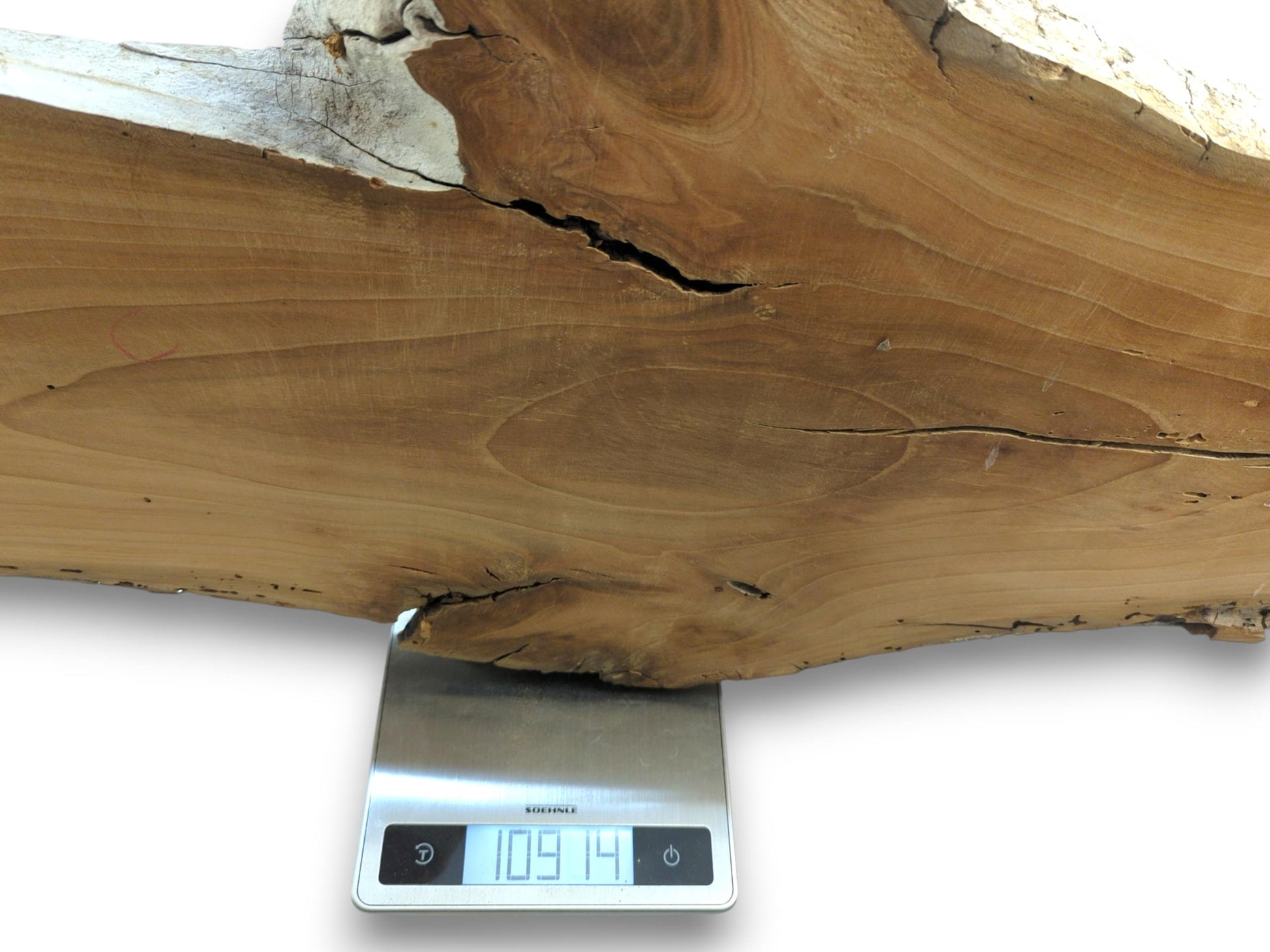 A thick, live edge cherry wood slab with visible cracks rests on a digital scale.
