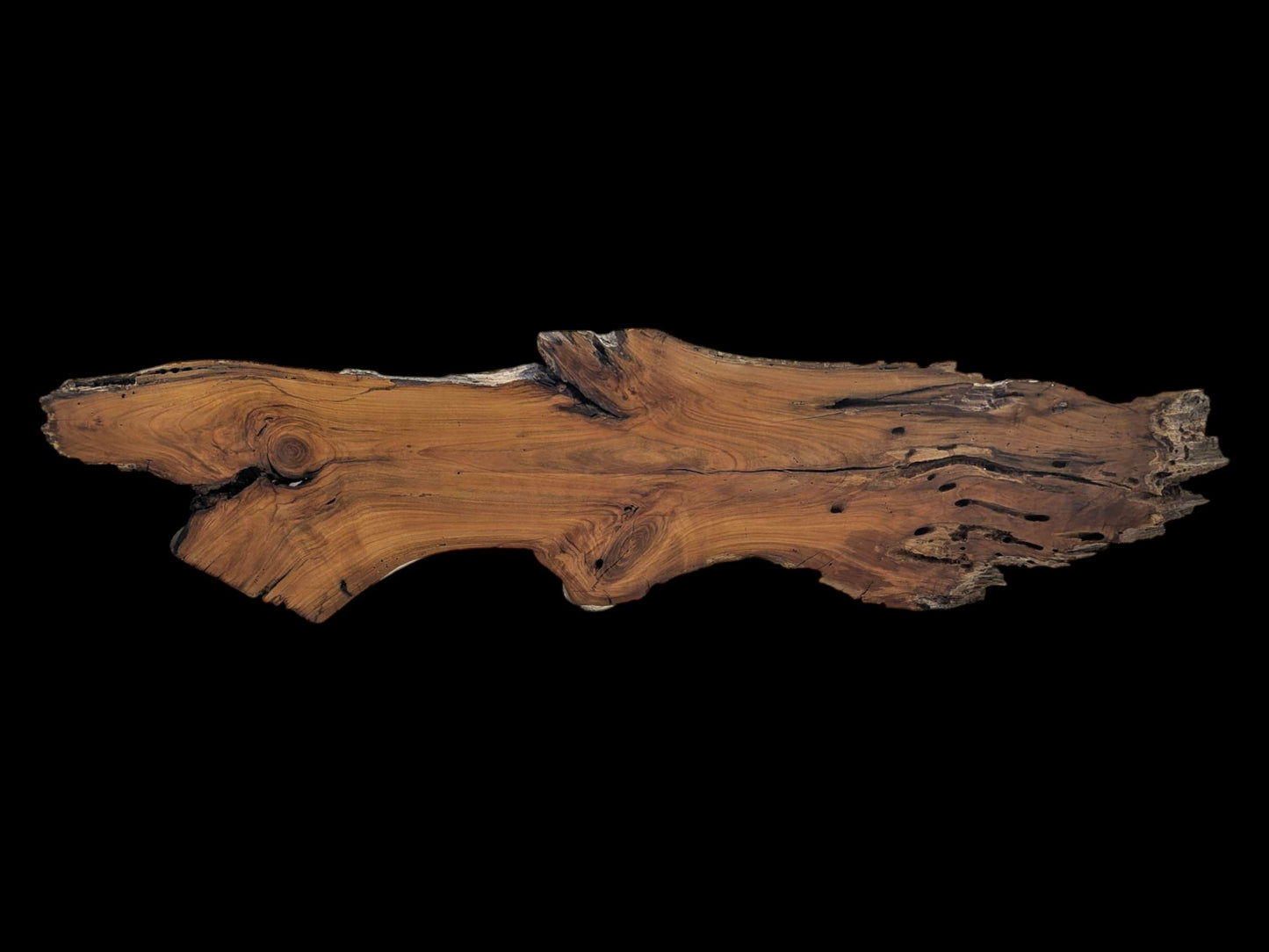 A long, live edge cherry wood slab with natural curves, visible knots, and holes.