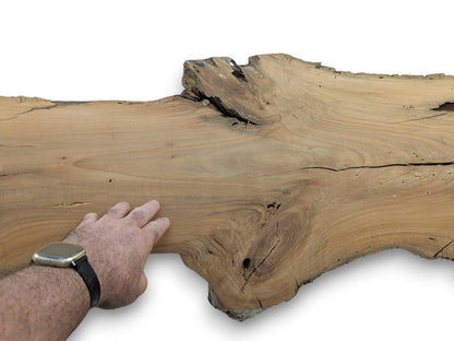 A person's hand with a watch touching a light brown cherry wood slab with a live edge.