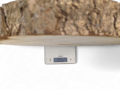 Underside of a natural wood slab with bark resting on a white digital scale showing "3964".