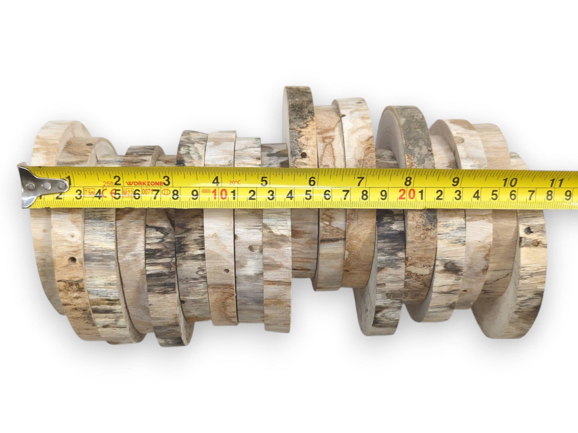 A yellow tape measure stretches horizontally across two rows of rustic, bark-covered lumber discs.