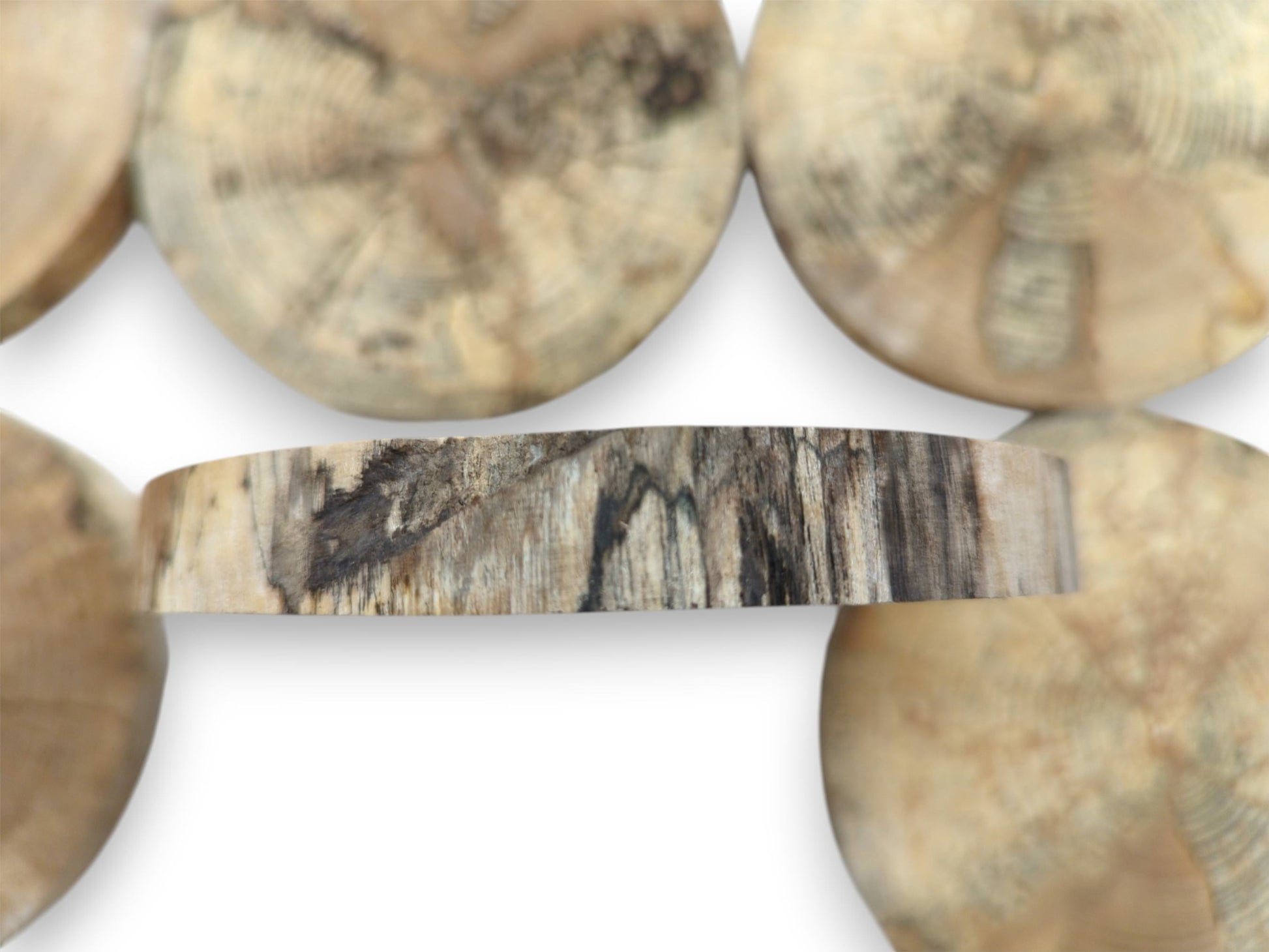 A spalted timber slice's edge reveals dark, vertical striations against a hazy, circular background.
