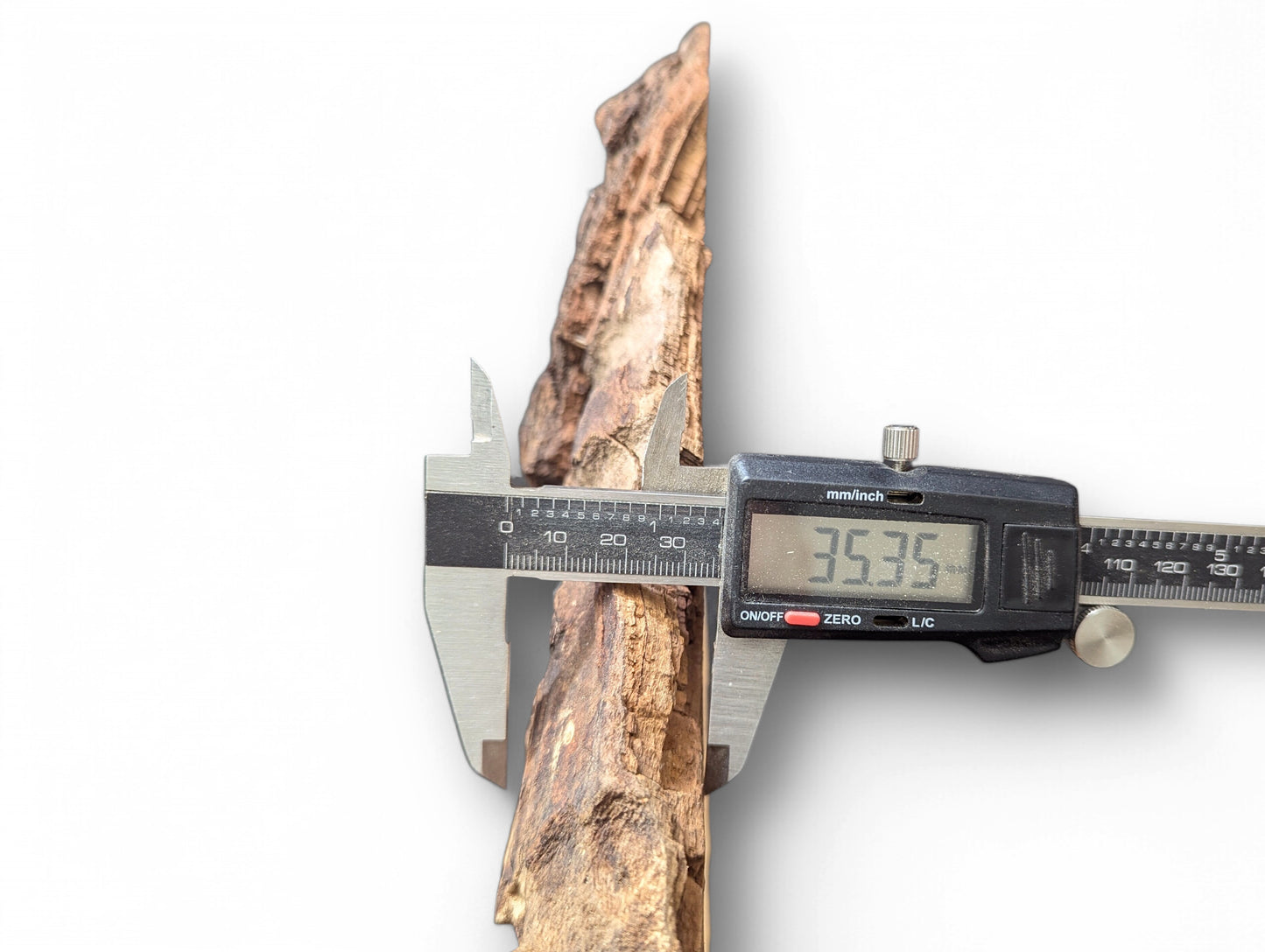 Digital caliper measuring a textured, light brown wood piece, displaying 35.35 mm on screen.