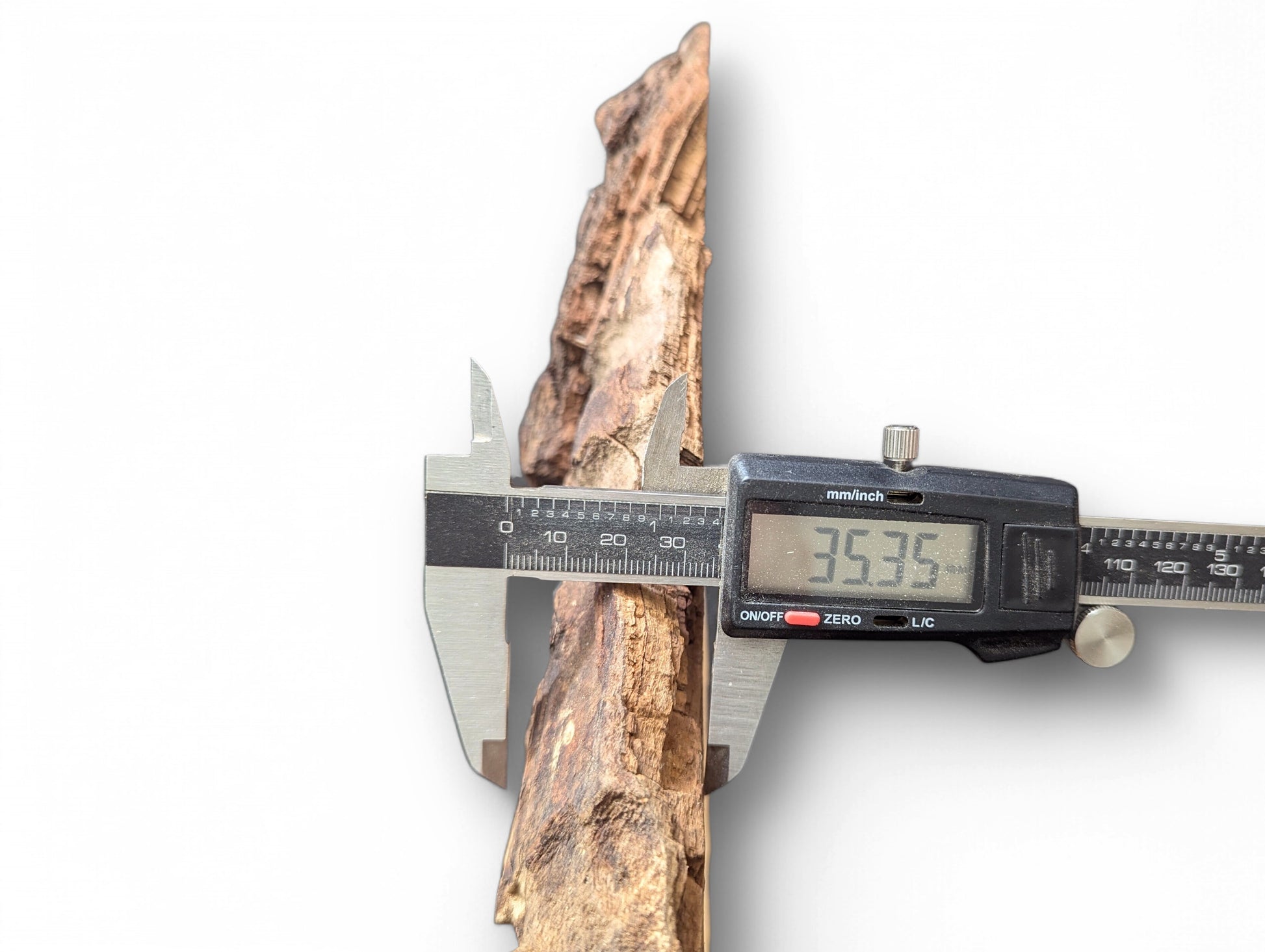 Digital caliper measuring a textured, light brown wood piece, displaying 35.35 mm on screen.