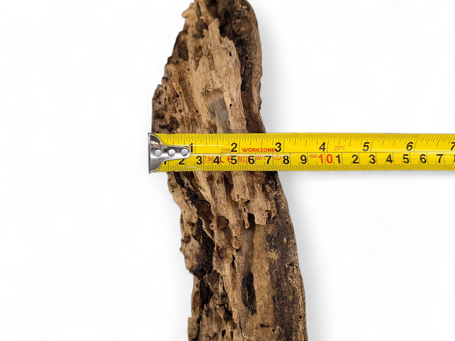 Rough, weathered brown wood with deep cracks, organic holes, horizontally measured by a yellow tape.