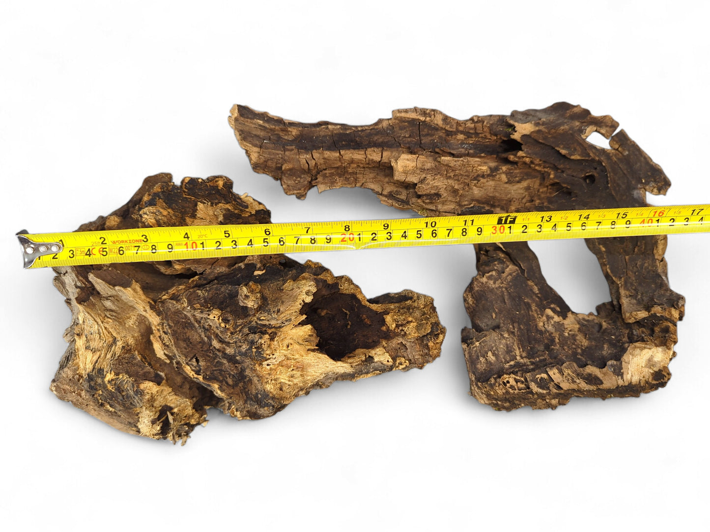 Two dark brown, hollow driftwood pieces with rough bark and exposed grain, measured by yellow tape.