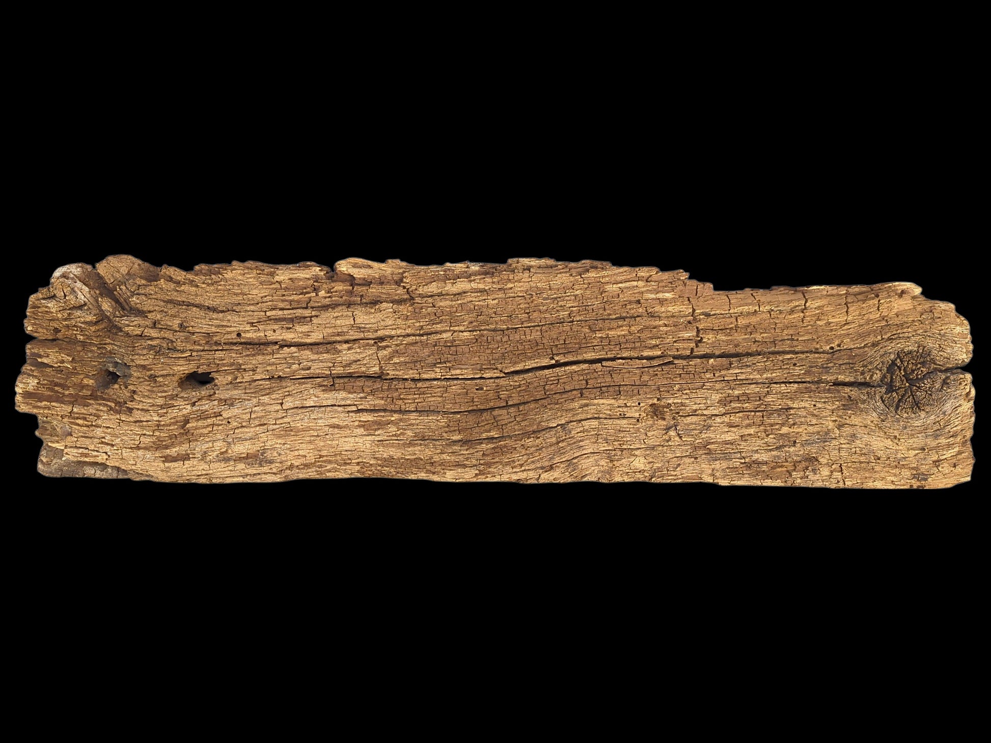 Horizontal brown wood fragment shows extensive cracks, a crumbly, flaking surface, and a knot.