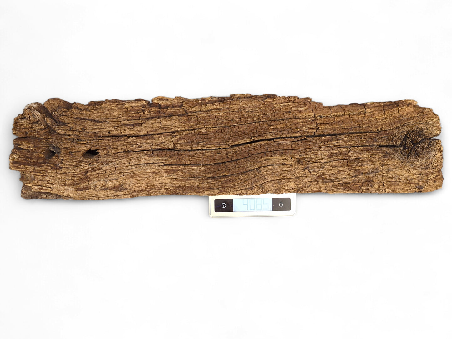 An elongated, rough brown wood fragment with deep cracks rests on a digital scale showing 408.5.