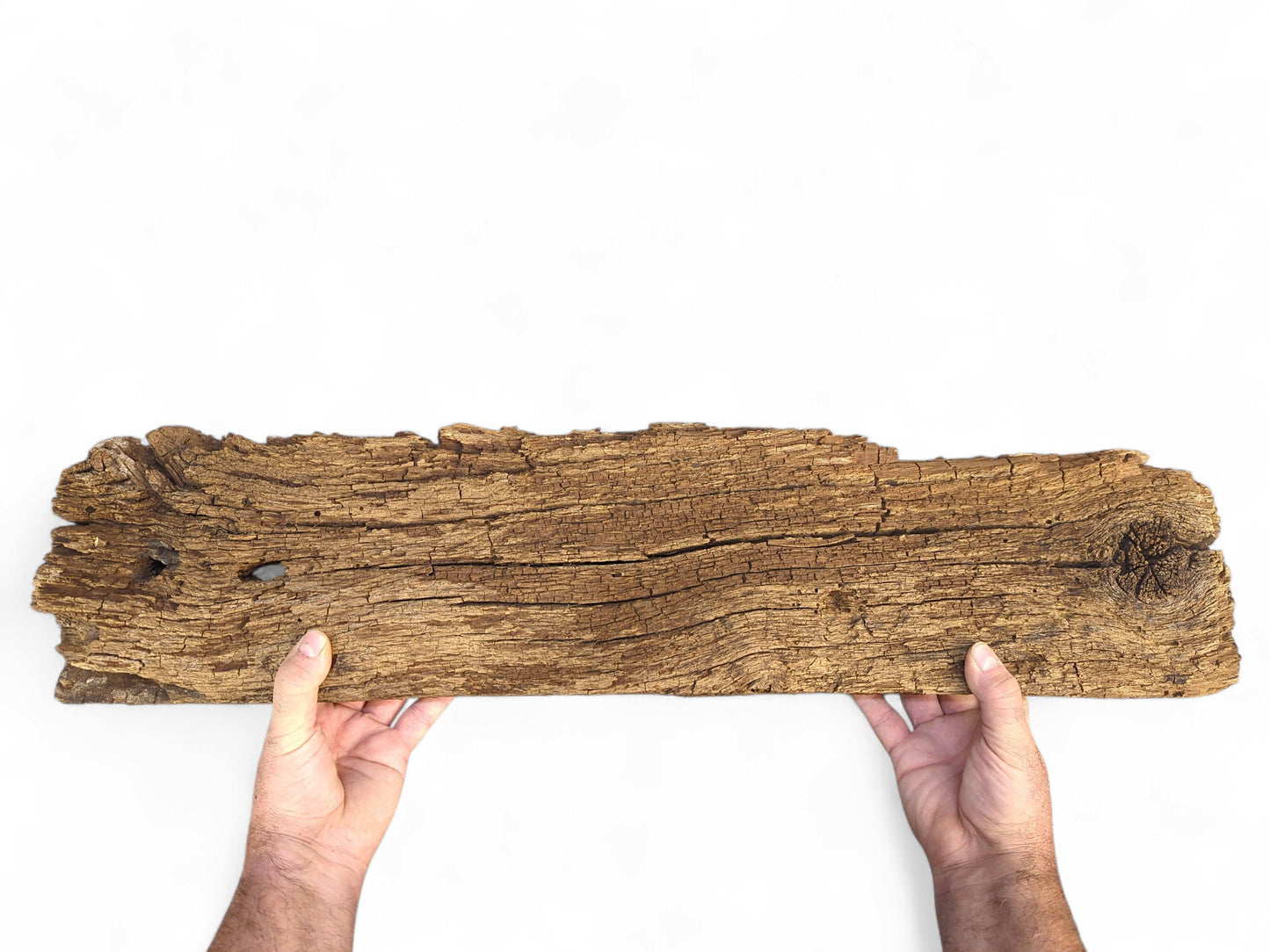 Two hands hold a deeply cracked, dark brown reclaimed wood fragment, featuring a flaking, crumbly surface.