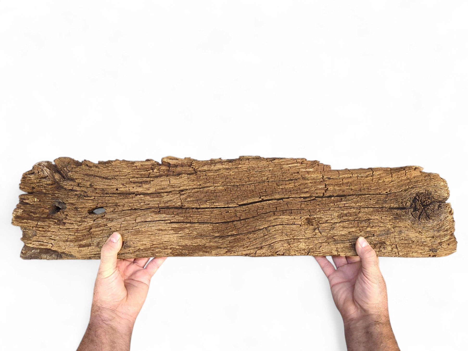 Two hands hold a deeply cracked, dark brown reclaimed wood fragment, featuring a flaking, crumbly surface.