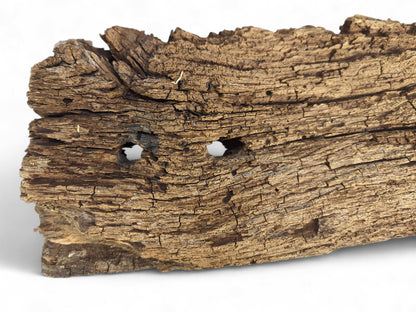 A brown, aged reclaimed wood fragment showing a flaking, deeply cracked surface and two holes.