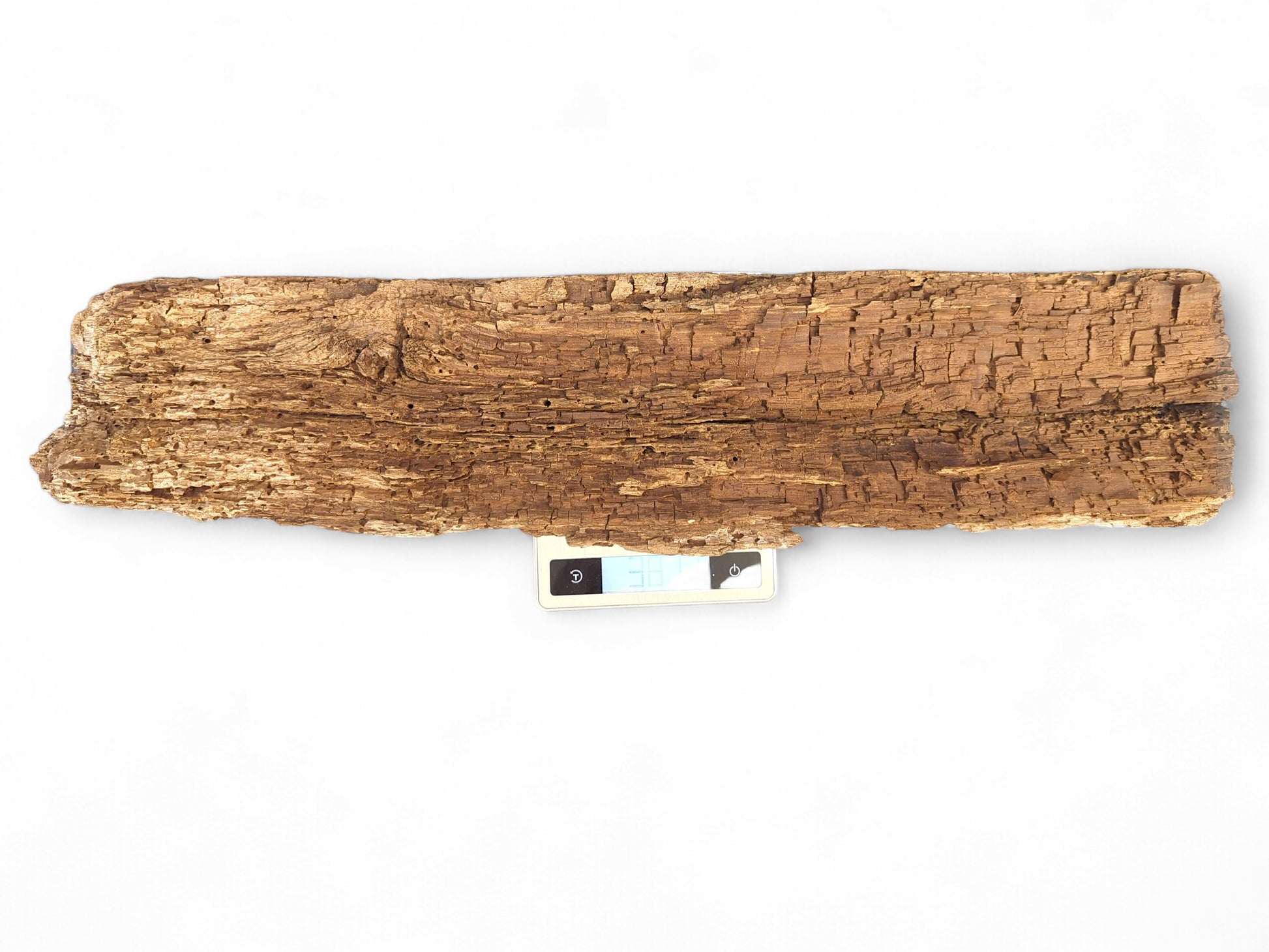 A rectangular, golden-brown wood fragment with a deeply flaking, crumbly surface, resting on a digital scale.