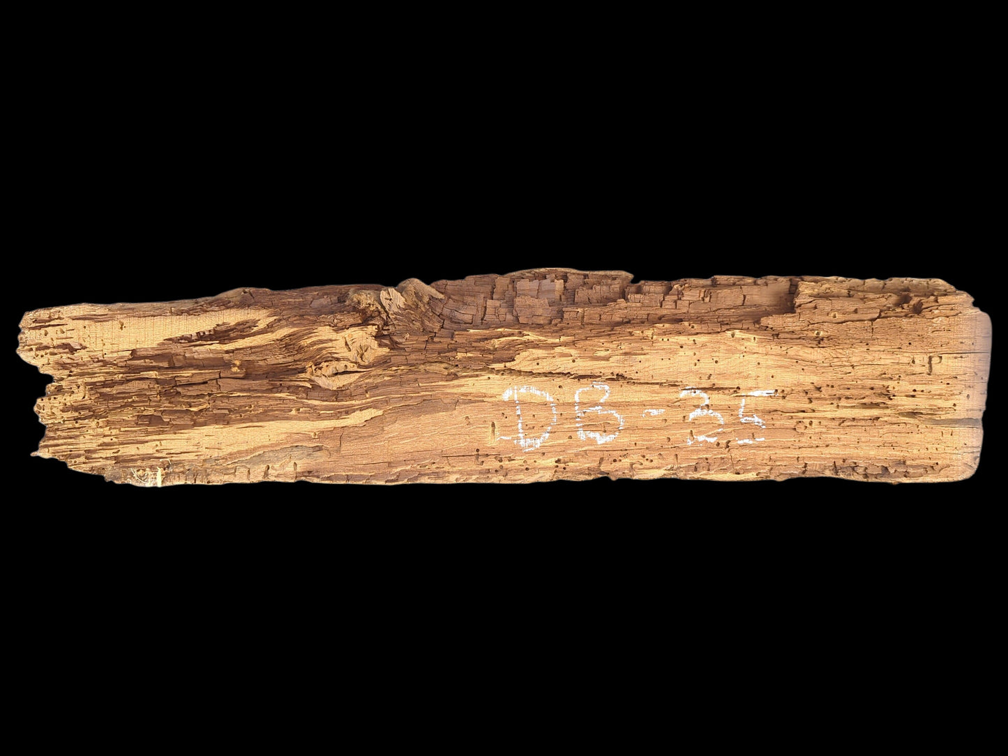 Elongated, light brown reclaimed wood fragment, deeply textured, extensively flaking, crumbly, with many small holes. "DB-35" marked.
